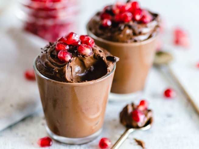Two small glasses of rich, dark chocolate mousse, topped with pomegranate seeds.