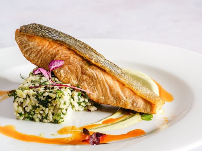 Pan-seared salmon fillet with a vibrant herb rice pilaf and creamy sauce, presented on a white plate.